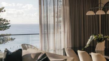 Ein modernes Wohnzimmer mit Meerblick, ein Essbereich mit Stühlen und ein Sofa mit Kissen.