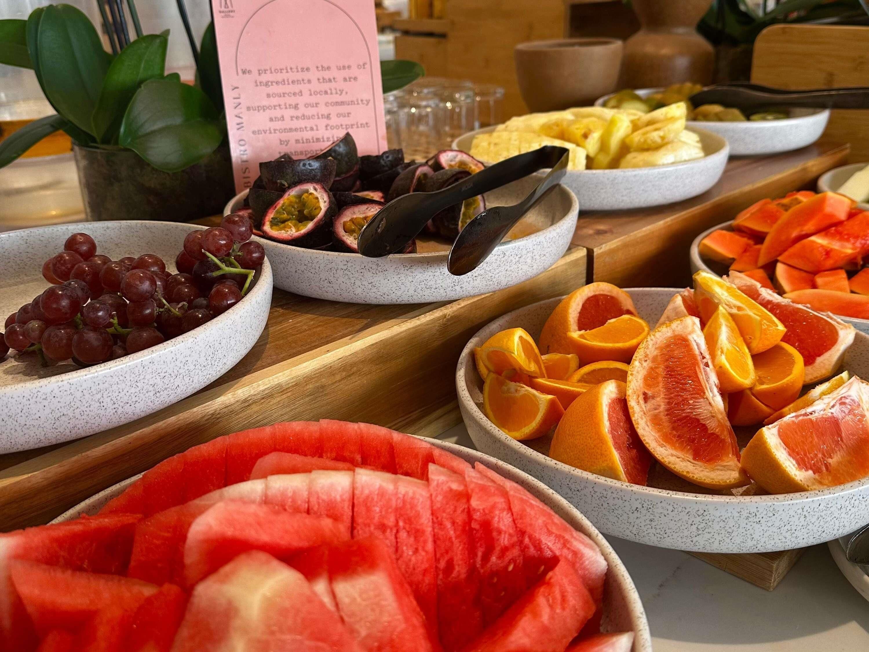 Una mesa de buffet con varias frutas y un cartel sobre abastecimiento local.