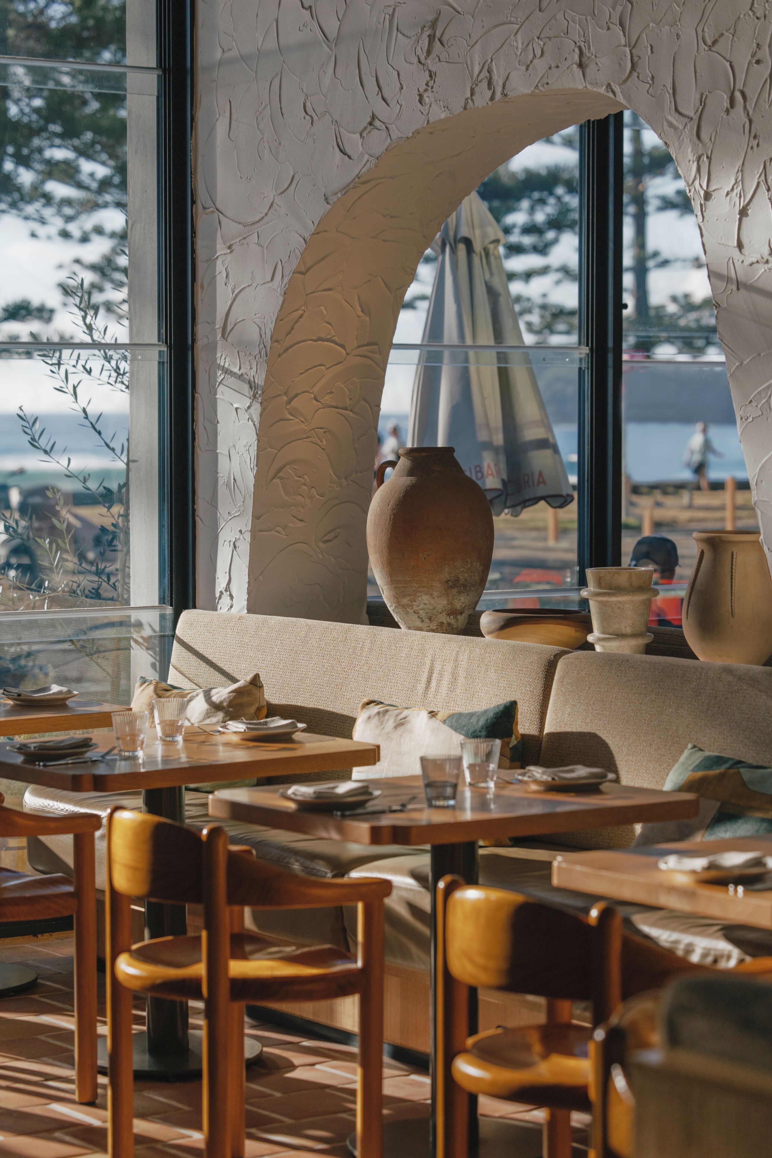 Interior de restaurante con un amplio ventanal arqueado, mesas y sillas de madera.