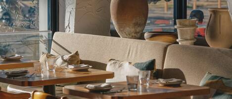 Interior de restaurante con un amplio ventanal arqueado, mesas y sillas de madera.