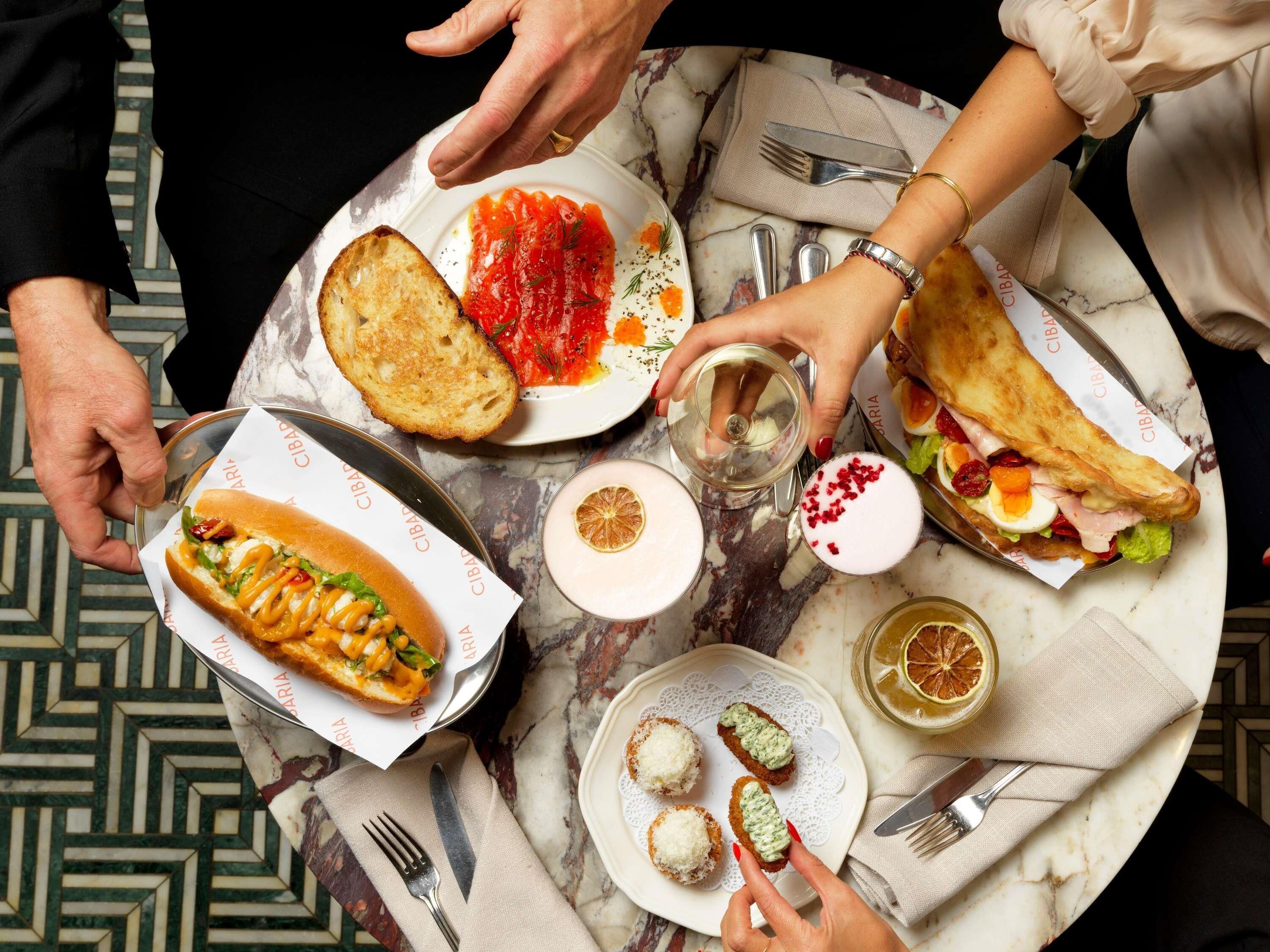 Una mesa con diferentes alimentos, incluyendo un sándwich, un perro caliente y un plato con salsa roja.