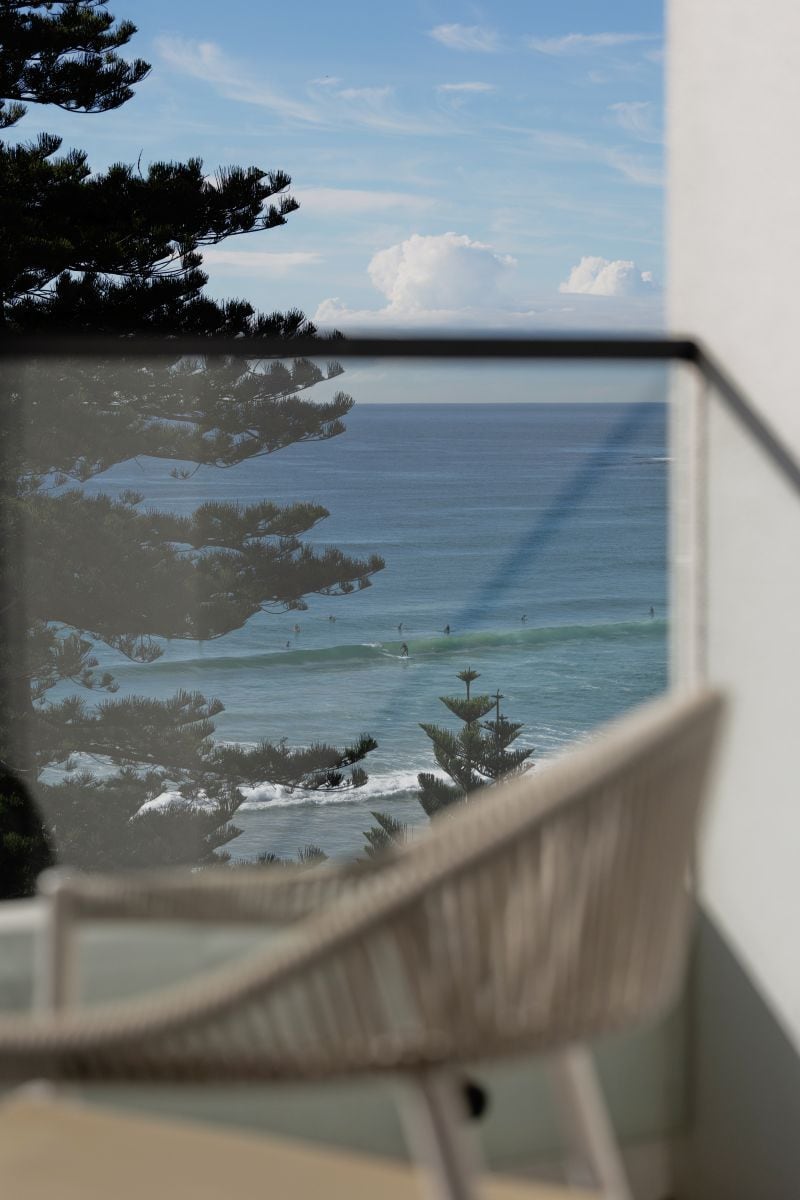 Une vue sur l’océan à travers une fenêtre, avec une chaise au premier plan.
