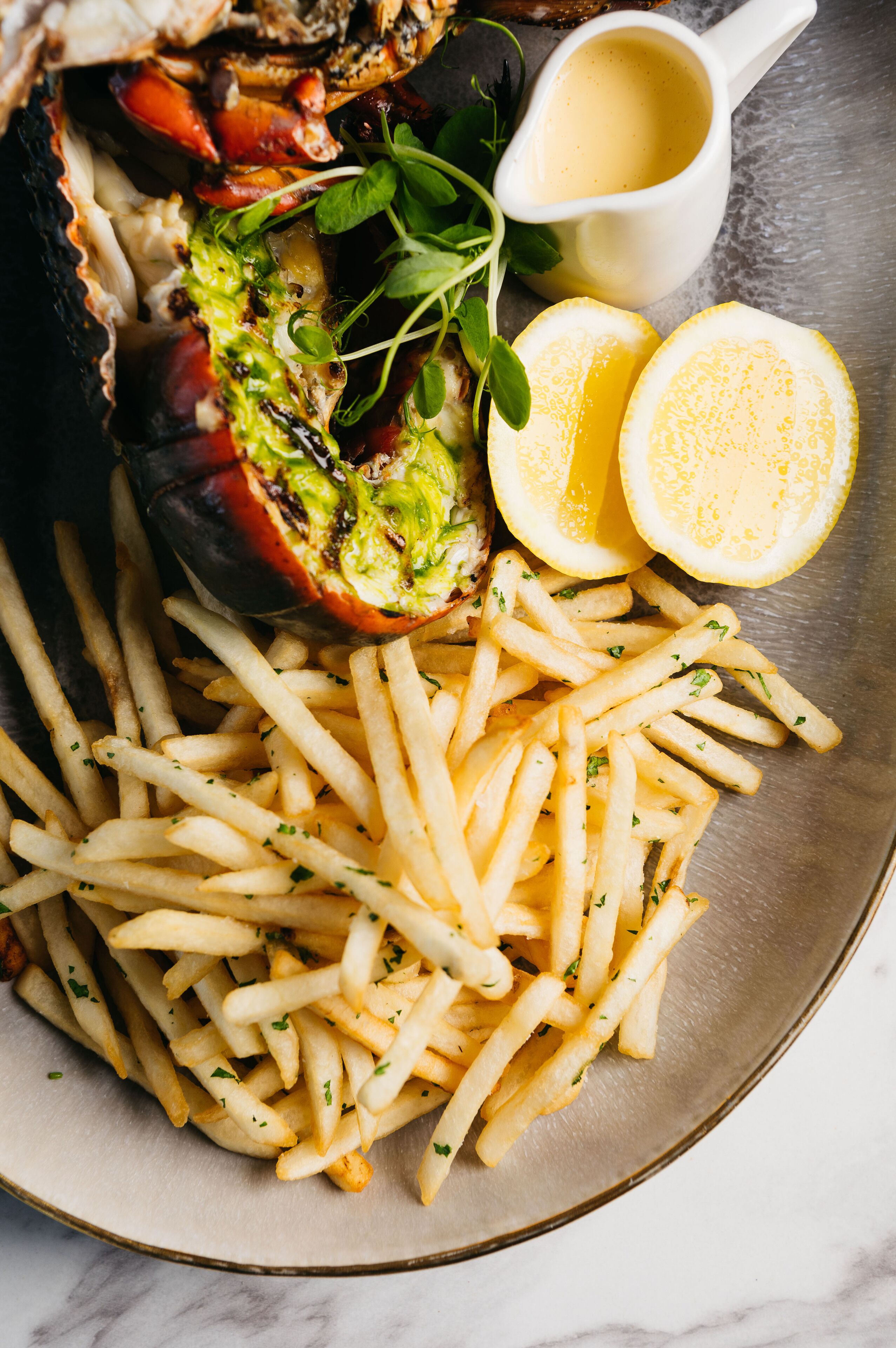 Une assiette de frites, accompagnée d’une sauce et de quartiers de citron.