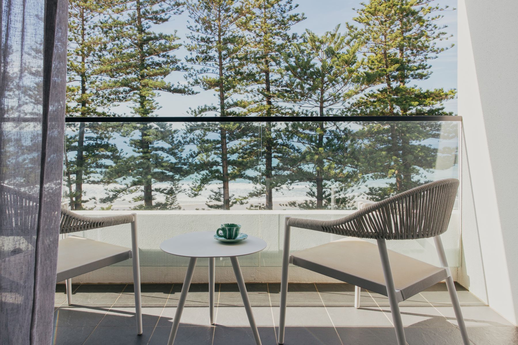 A balcony with two wicker chairs and a small round table, overlooking a forested area.