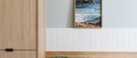 A wooden cabinet, a framed coastal landscape painting, and two ceramic containers on a wooden shelf.