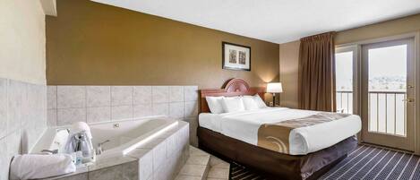 A hotel room with a large bed, a separate bathtub, and a view of the outdoors through a sliding door.