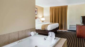 A hotel room with a large bathtub, a bed with a headboard, a television, and a desk with a chair.