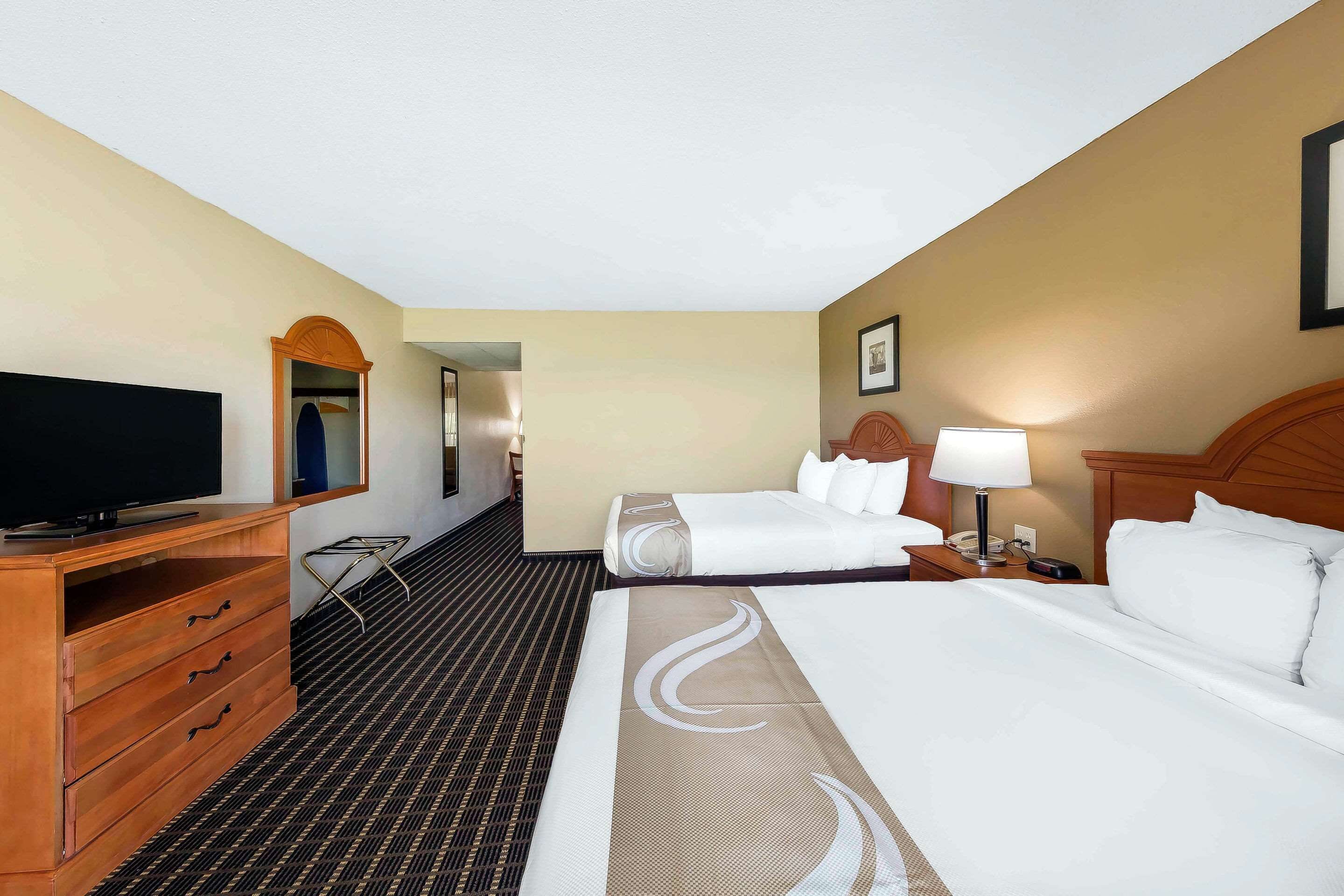 Une chambre d’hôtel avec un lit, une télévision, une commode et une lampe.