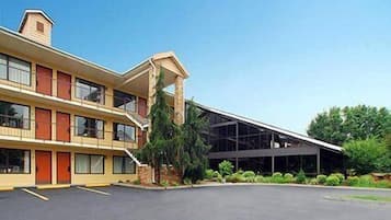 Un motel de dos pisos con una escalera central, un espacio exterior cubierto y un estacionamiento.