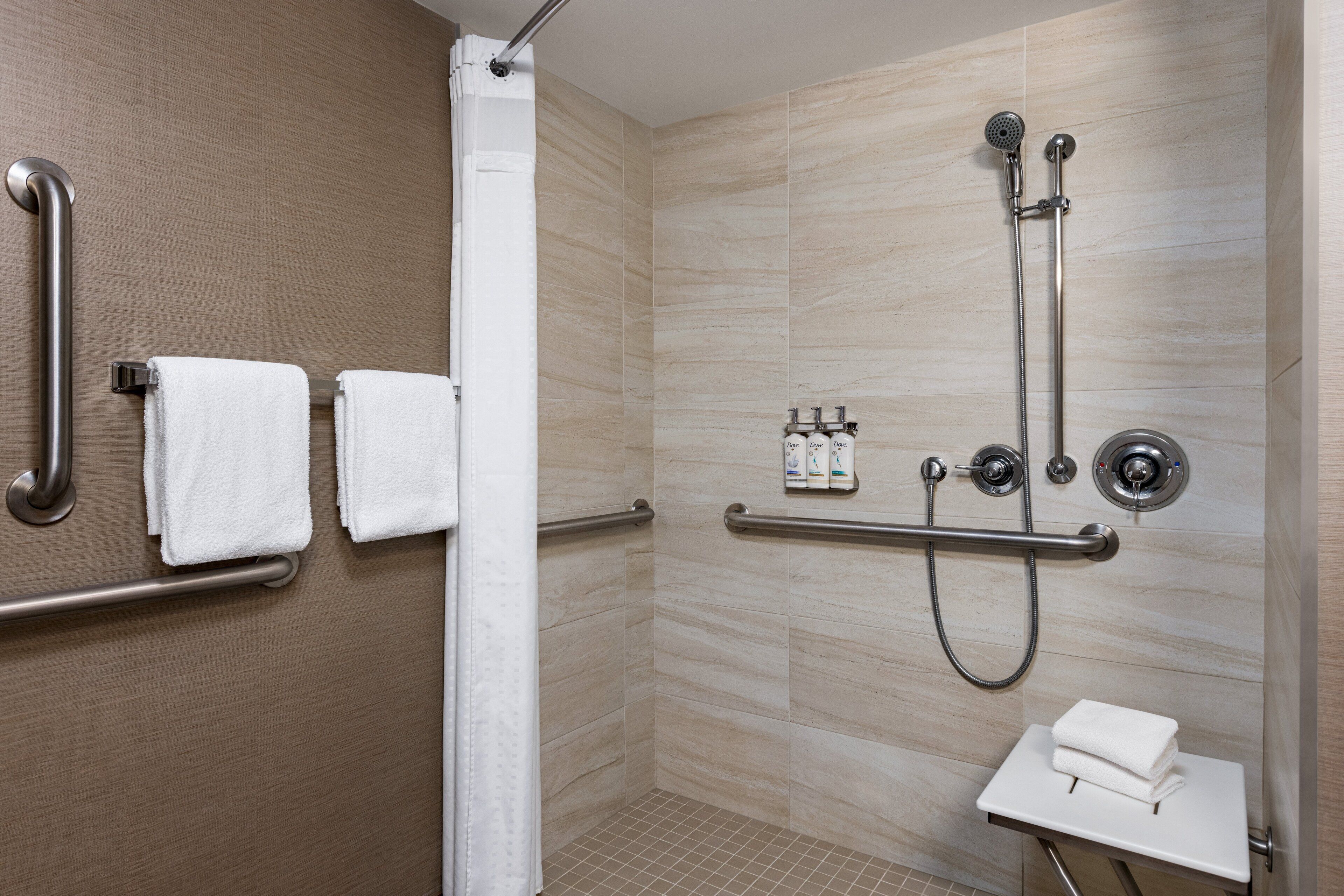 A modern shower area with grab bars, a showerhead, and a small sink with a towel.