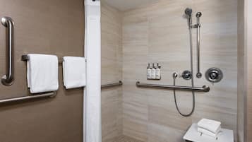 A modern shower area with grab bars, a showerhead, and a small sink with a towel.