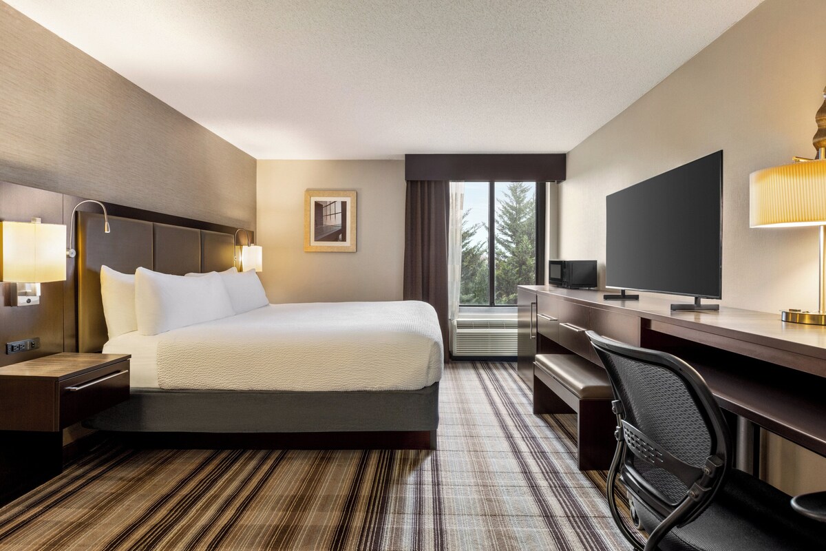 A hotel room with a bed, desk, chair, and large window.