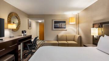 Habitación de hotel con cama, escritorio con silla, sofá, televisión y un cuadro en la pared.