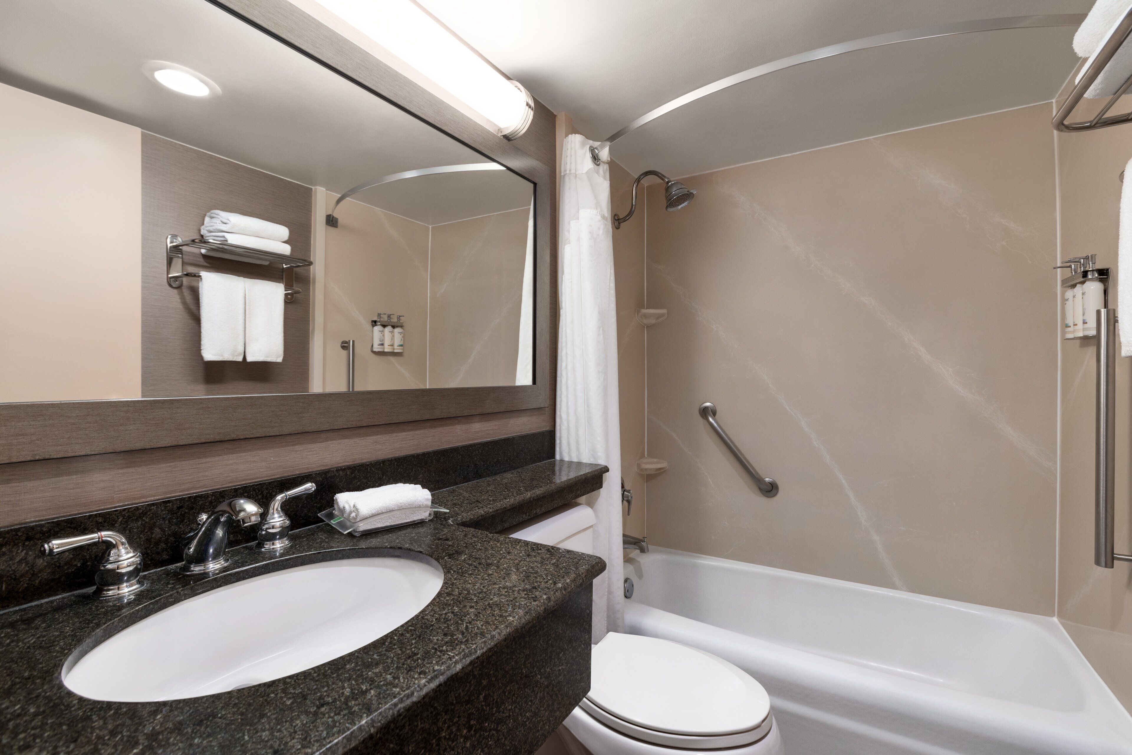 Un bagno moderno con lavabo su piano in granito, un water bianco e una vasca da bagno.