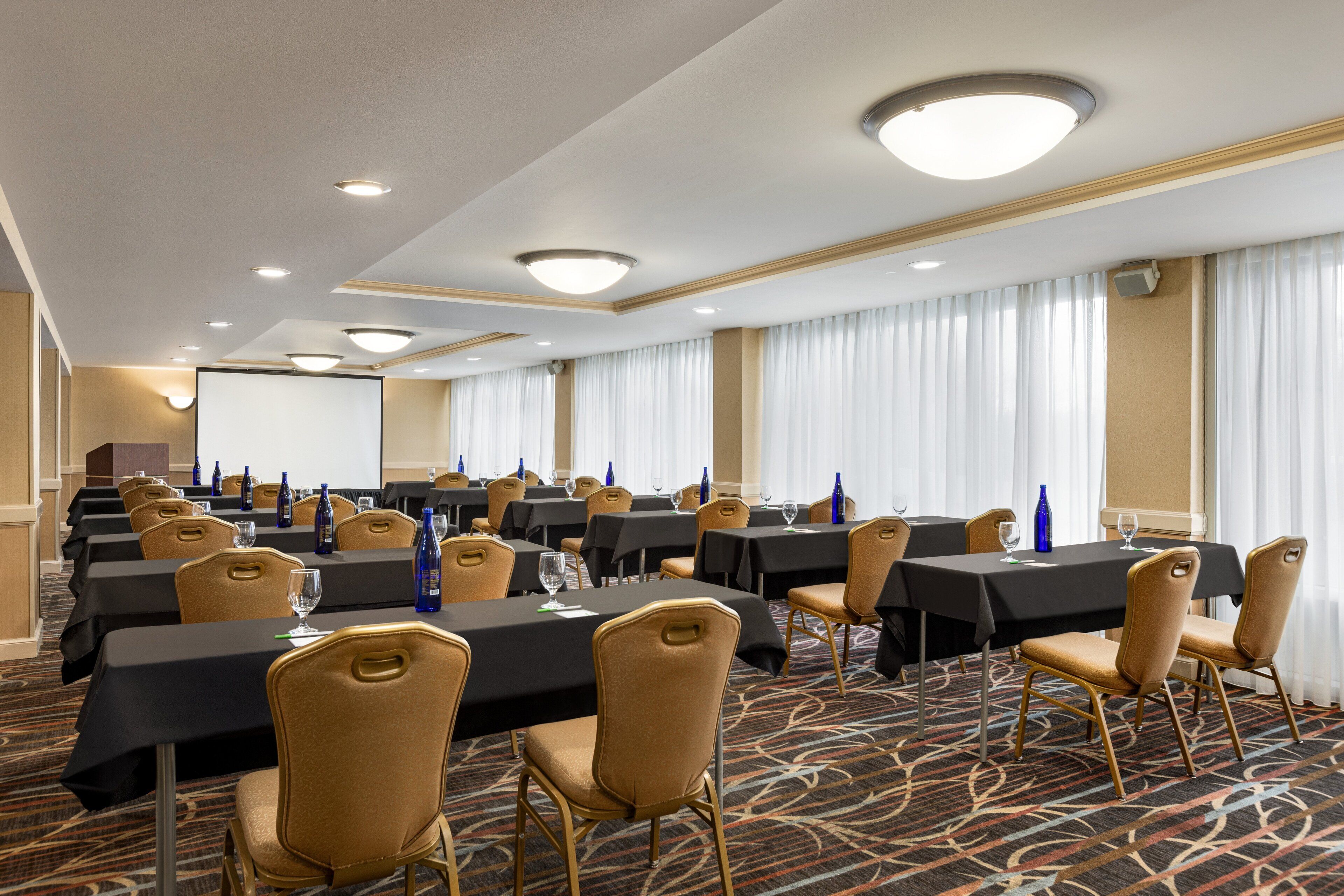 A conference room with multiple tables, chairs, and a projector screen.