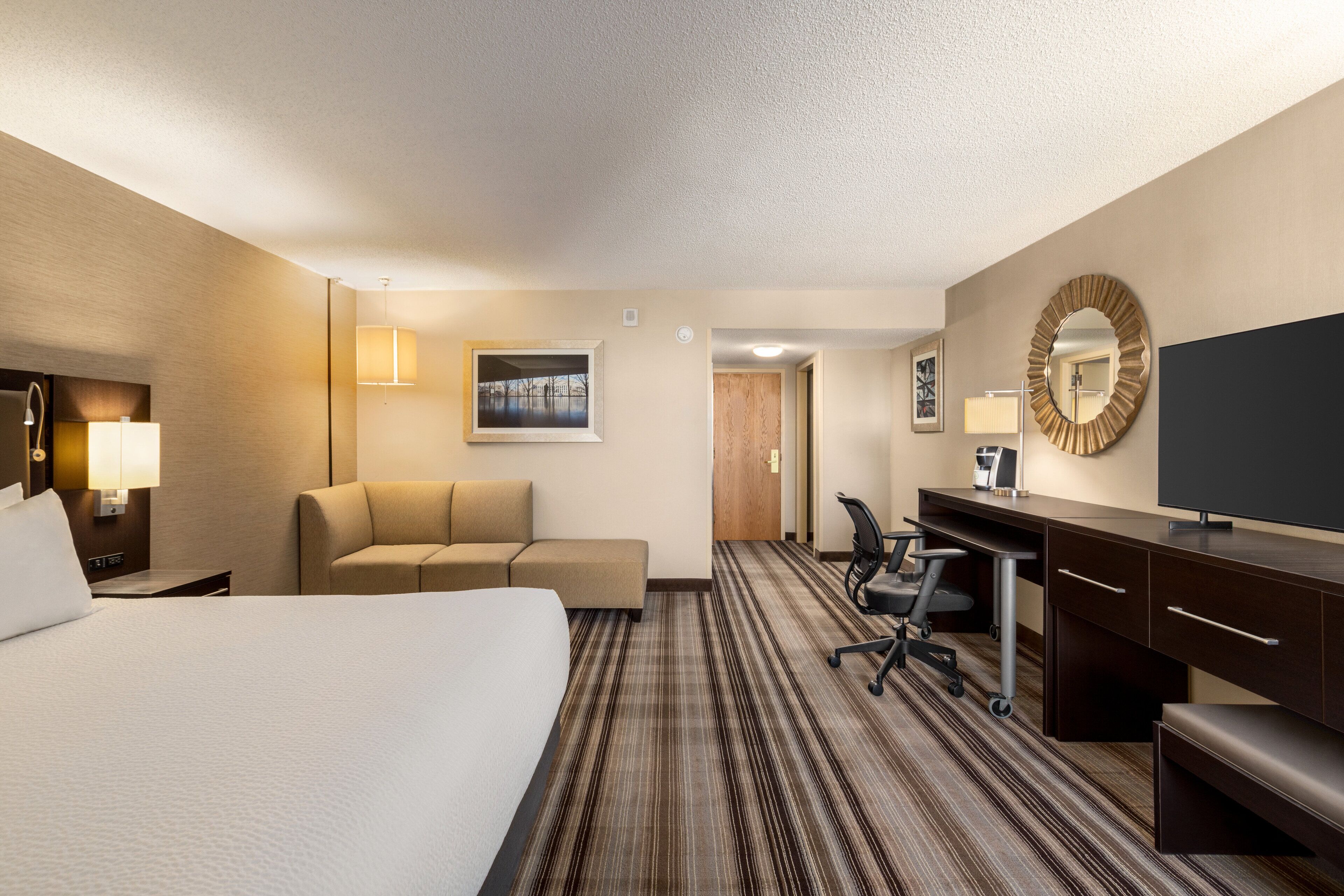 Une chambre d’hôtel avec un grand lit, un canapé, un bureau avec une chaise, une télévision et un miroir.