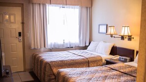 Habitación de hotel con dos camas, un escritorio, una silla, un ventanal con cortinas y dos lámparas fijadas a la pared.