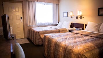 A hotel room with two beds, a television, a desk with a lamp, and a window with curtains.