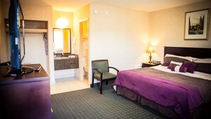 Habitación de hotel con cama, una silla, escritorio con computadora y baño visible a través de una puerta abierta.