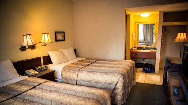 A hotel room with two beds, a bedside table with a phone, a nightstand, a bathroom with a sink and mirror, and a TV. - Langley Hwy Hotel (Langley)