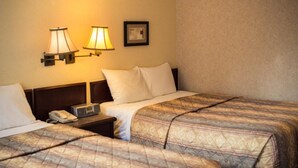 Habitación de hotel con dos camas, una mesita de noche con lámpara y un cuadro enmarcado en la pared.