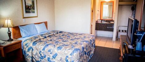 Habitación de hotel con cama, escritorio con lámpara, cómoda, espejo, televisión y cafetera.