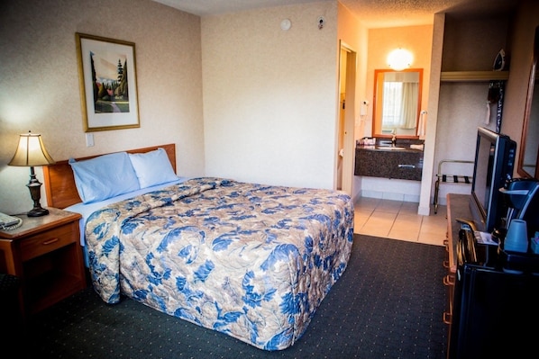 Habitación de hotel con cama, escritorio con lámpara, cómoda, espejo, televisión y cafetera.