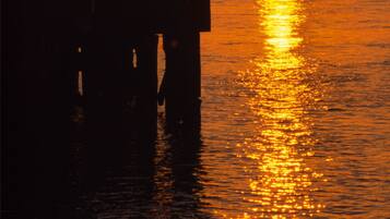 Un muelle con un pabellón y sillas que da vista a un atardecer sobre un río con un puente al fondo.