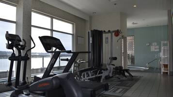 A gym with cardio machines, weightlifting equipment, and a view of a body of water through large windows.