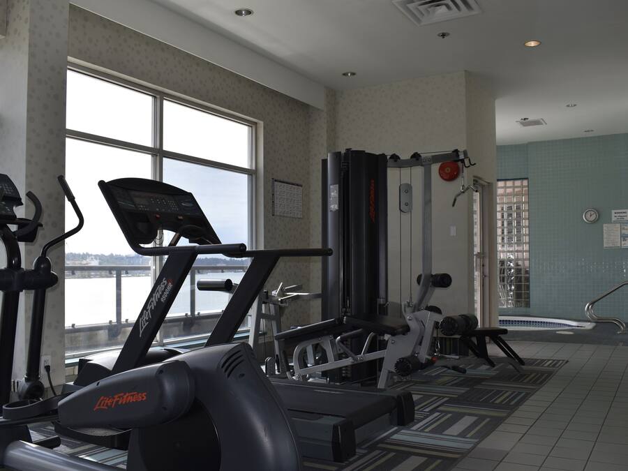 A gym with cardio machines, weightlifting equipment, and a view of a body of water through large windows.