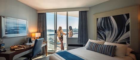Habitación de hotel con una cama grande, un escritorio con lámpara, una silla y vista al exterior a través de una puerta corrediza.