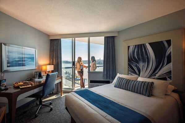 A hotel room with a large bed, a desk with a lamp, a chair, and a view of the outdoors through a sliding door.