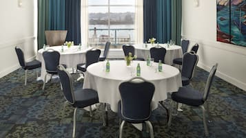 A conference room with round tables, chairs, and a view of a body of water through large windows.