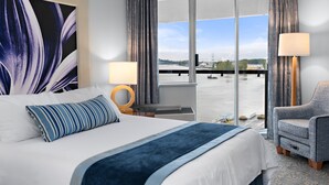 Habitación de hotel con una cama grande, una silla, un escritorio y vista a un cuerpo de agua a través de una ventana.