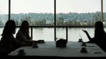 A view through a window with a table and chairs facing a body of water and a forested area.