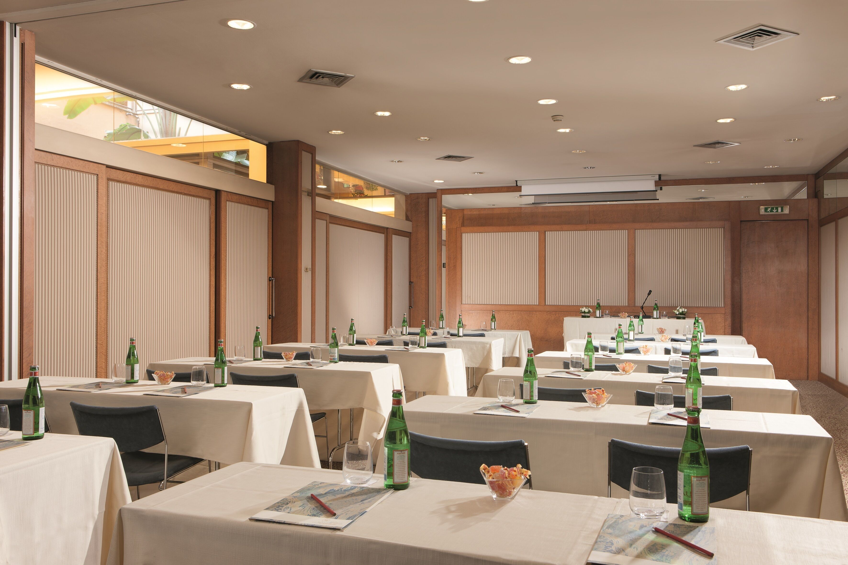 A conference room with tables set for a meeting, equipped with microphones and a projector screen.