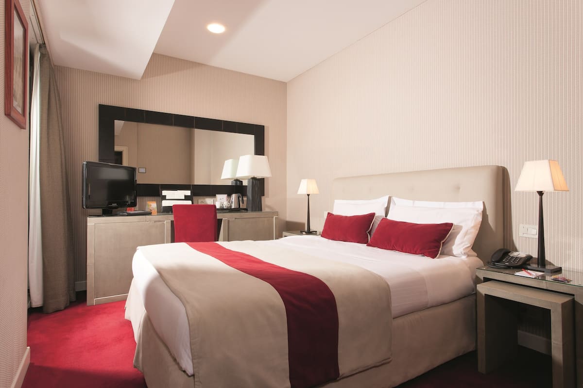 A hotel room with a large bed, two bedside tables with lamps, a desk with a television, and a mirror above the desk.