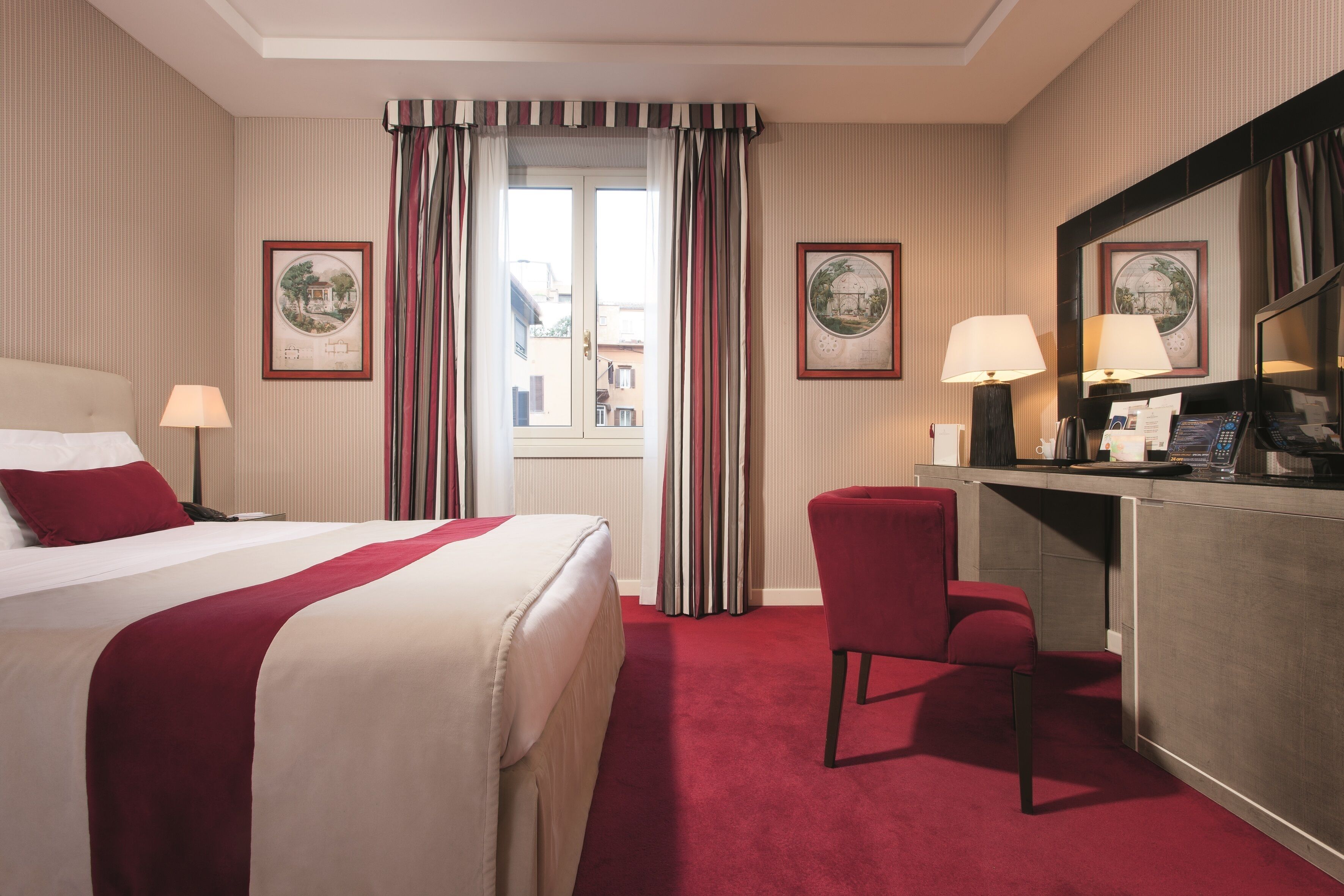 A hotel room with a bed, desk, chair, and two framed pictures on the wall.