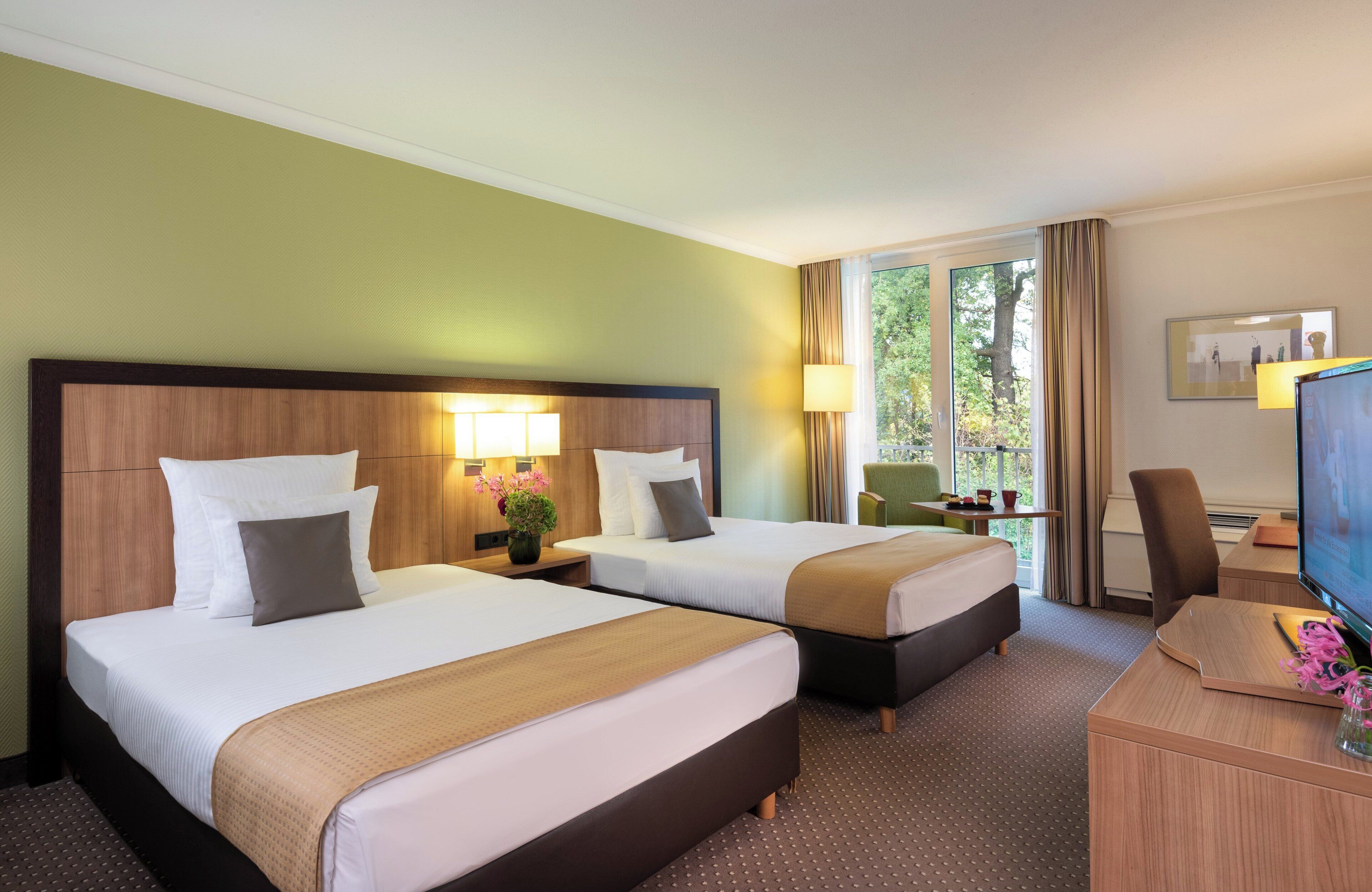 Habitación de hotel con dos camas, un escritorio con televisor y una ventana con cortinas.