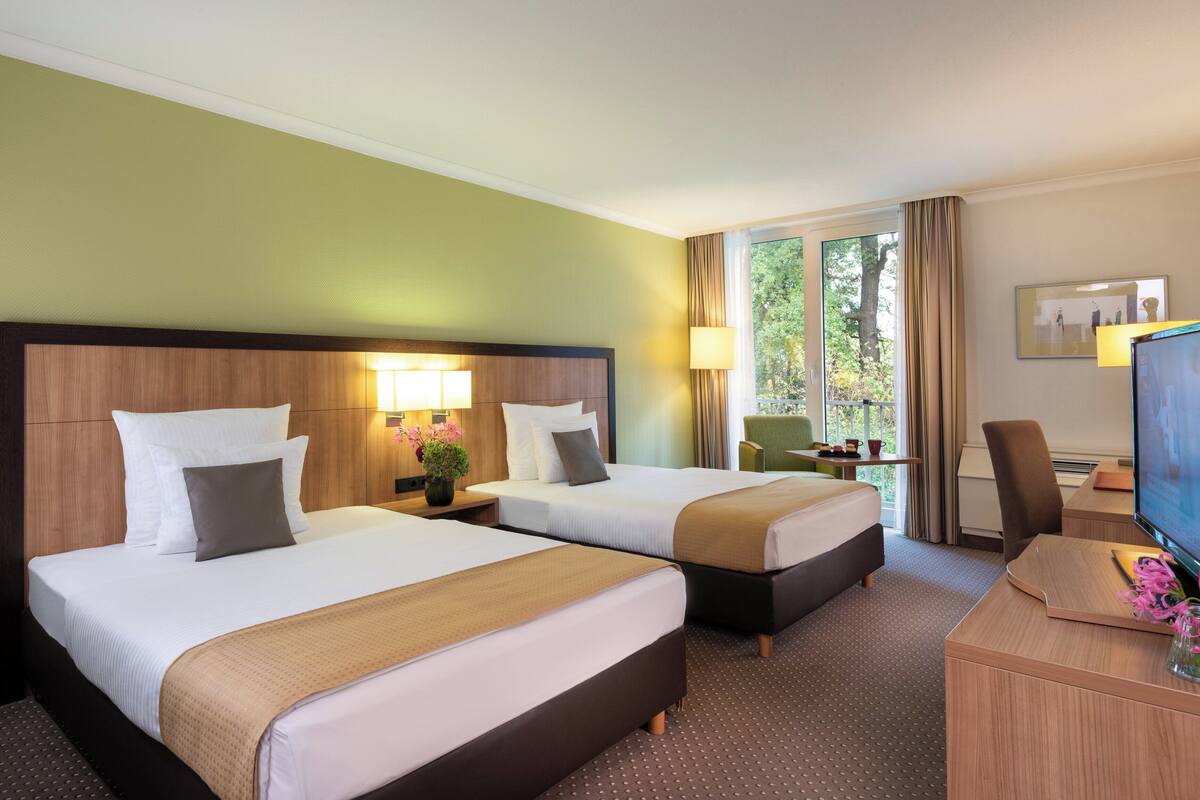 Habitación de hotel con dos camas, un escritorio con televisor y una ventana con cortinas.