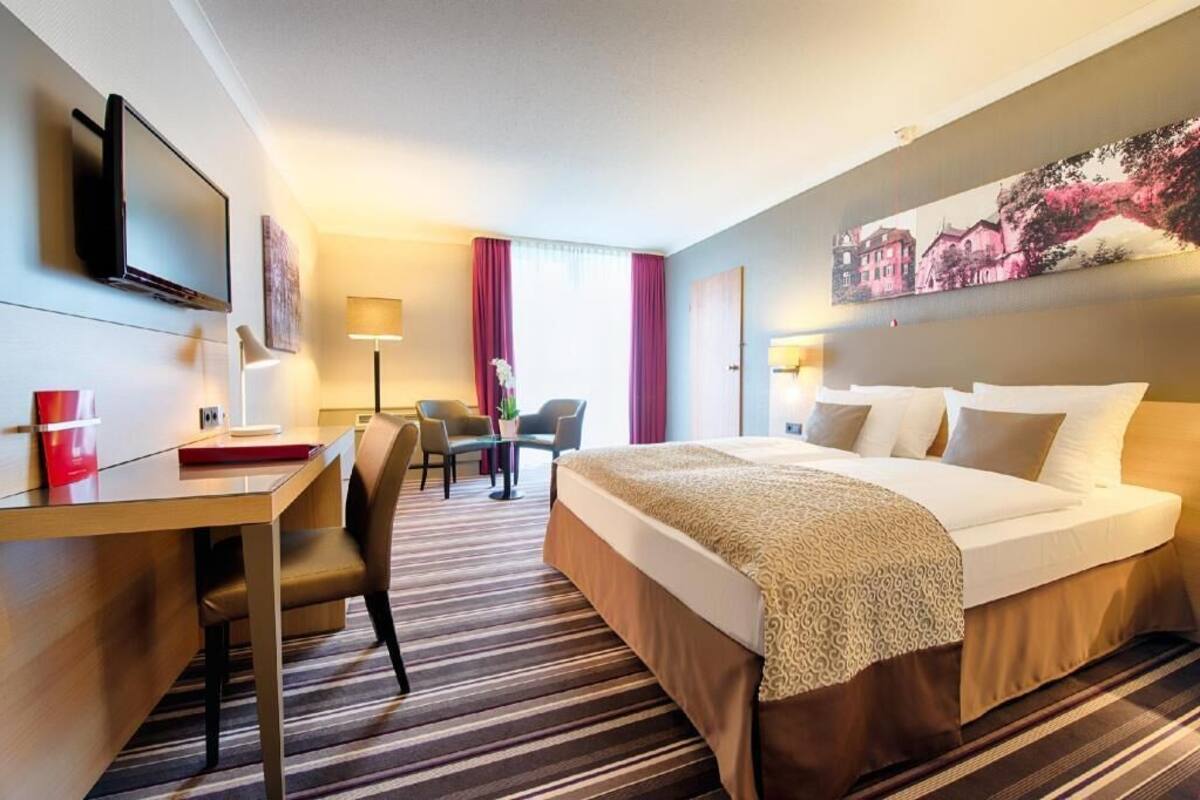Habitación de hotel con cama, escritorio, sillas, televisor y un cuadro en la pared.