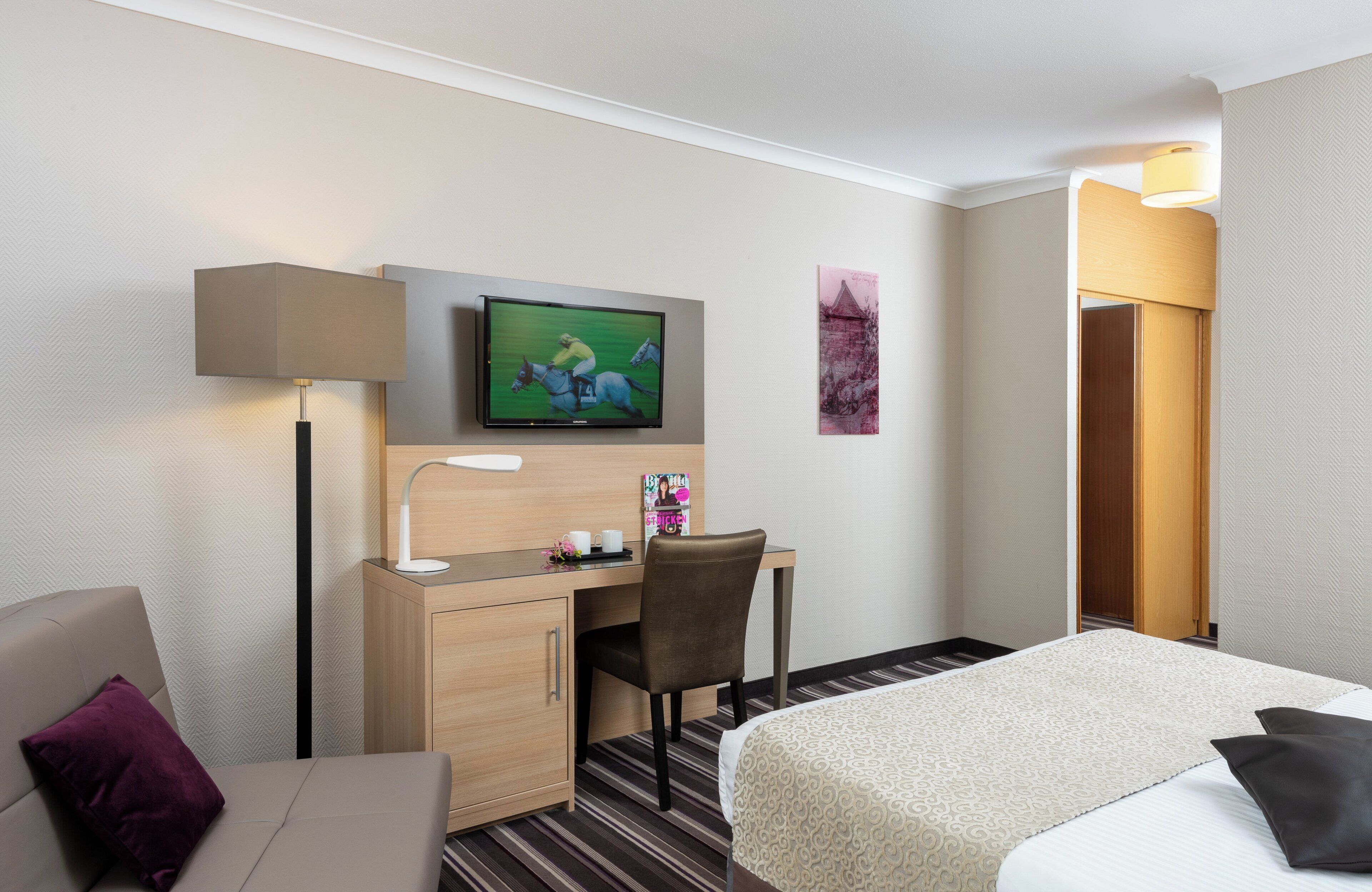 Una habitación de hotel con una cama, un escritorio con silla, un televisor y una lámpara.