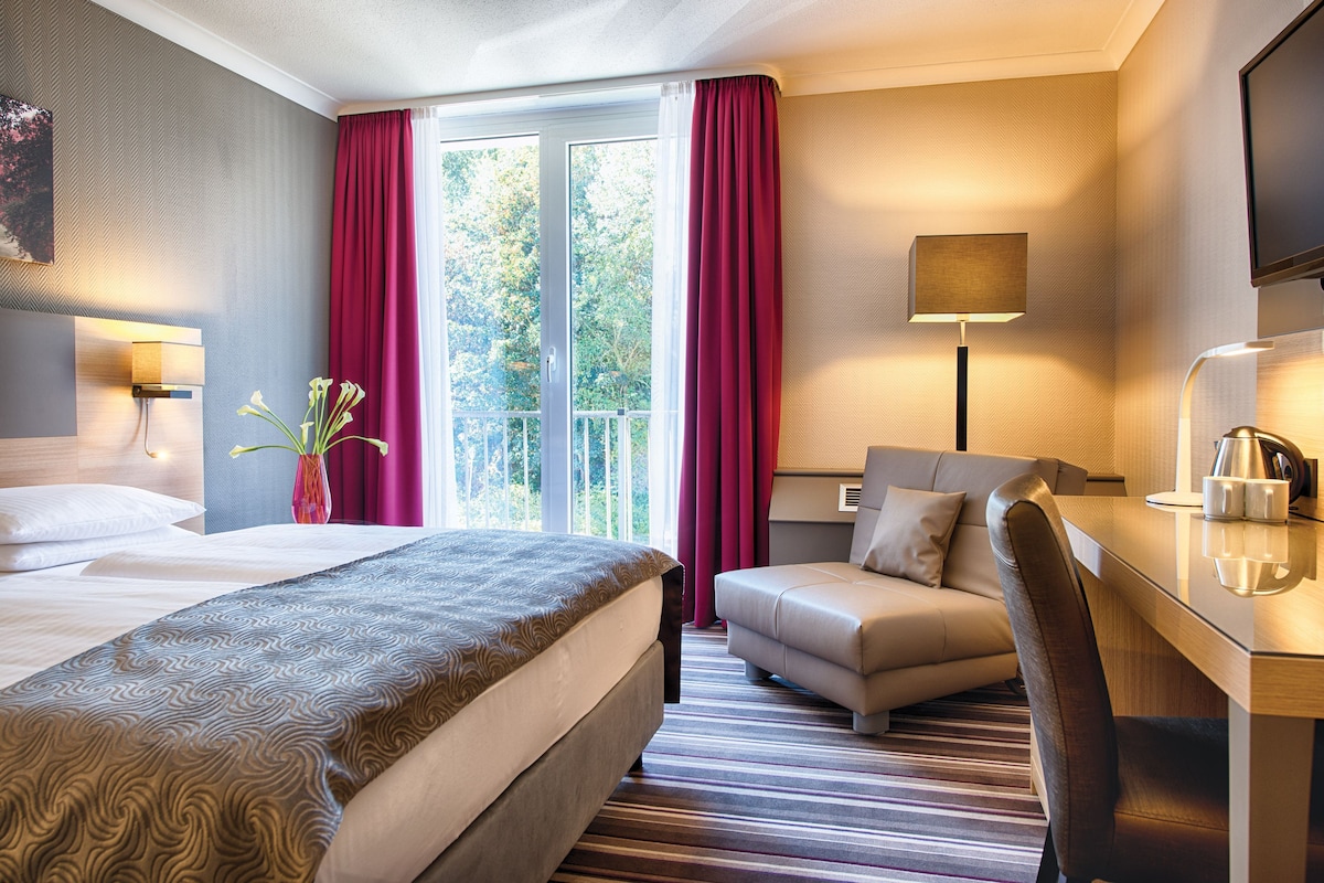 Una habitación de hotel con una cama, un escritorio, una silla, una lámpara y un televisor.