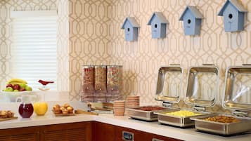 A breakfast buffet with various food items, a fruit bowl, and decorative birdhouses on the wall.