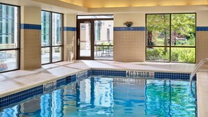 An indoor swimming pool with clear blue water, tiled walls, and large windows offering views of the outdoors.
