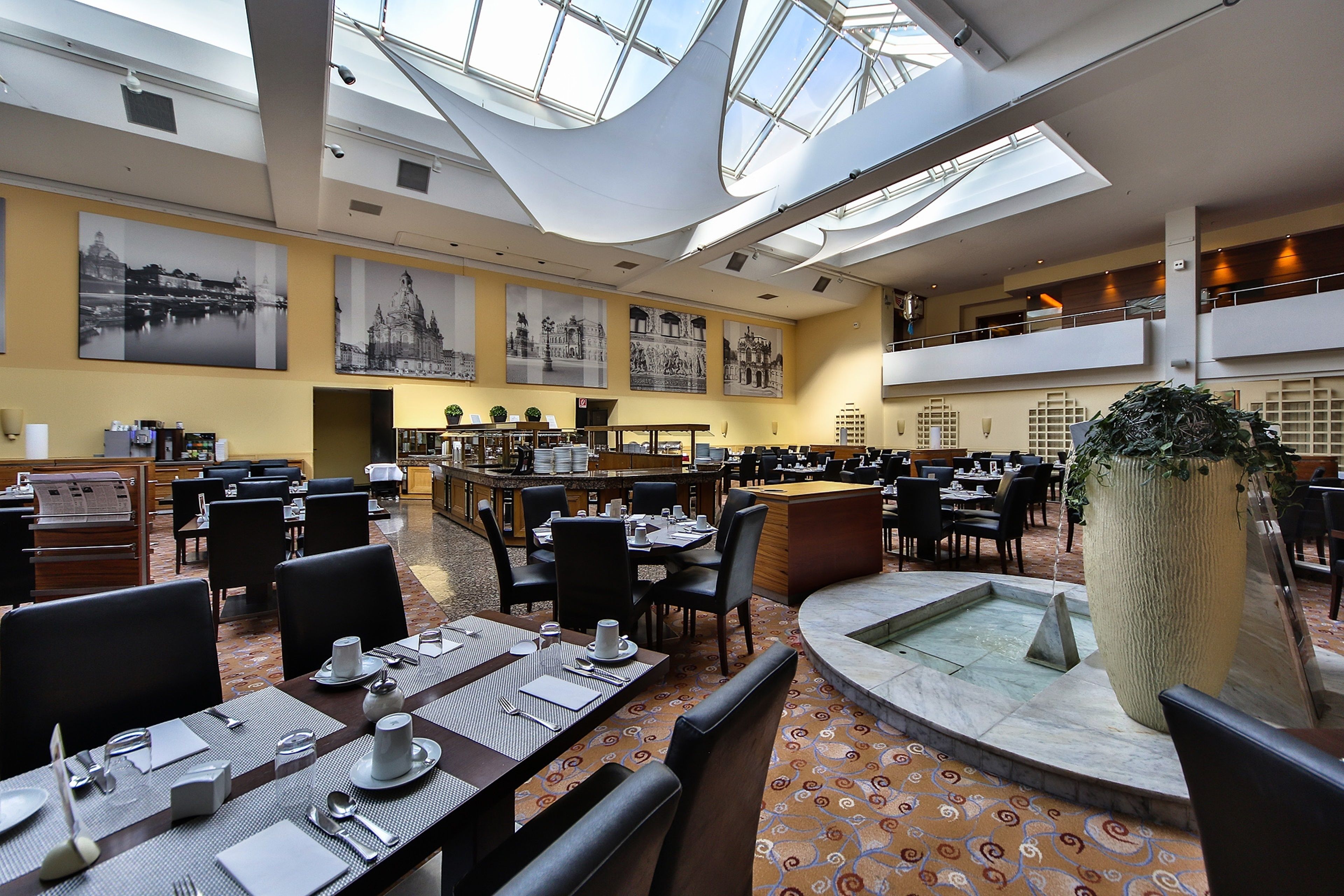 A spacious hotel lobby with high ceilings, a central fountain, and multiple dining areas.