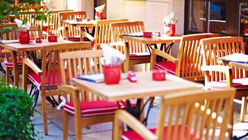 Ein Straßencafé mit Holztischen und -stühlen, roten Kissen und roten Gewürzbehältern.