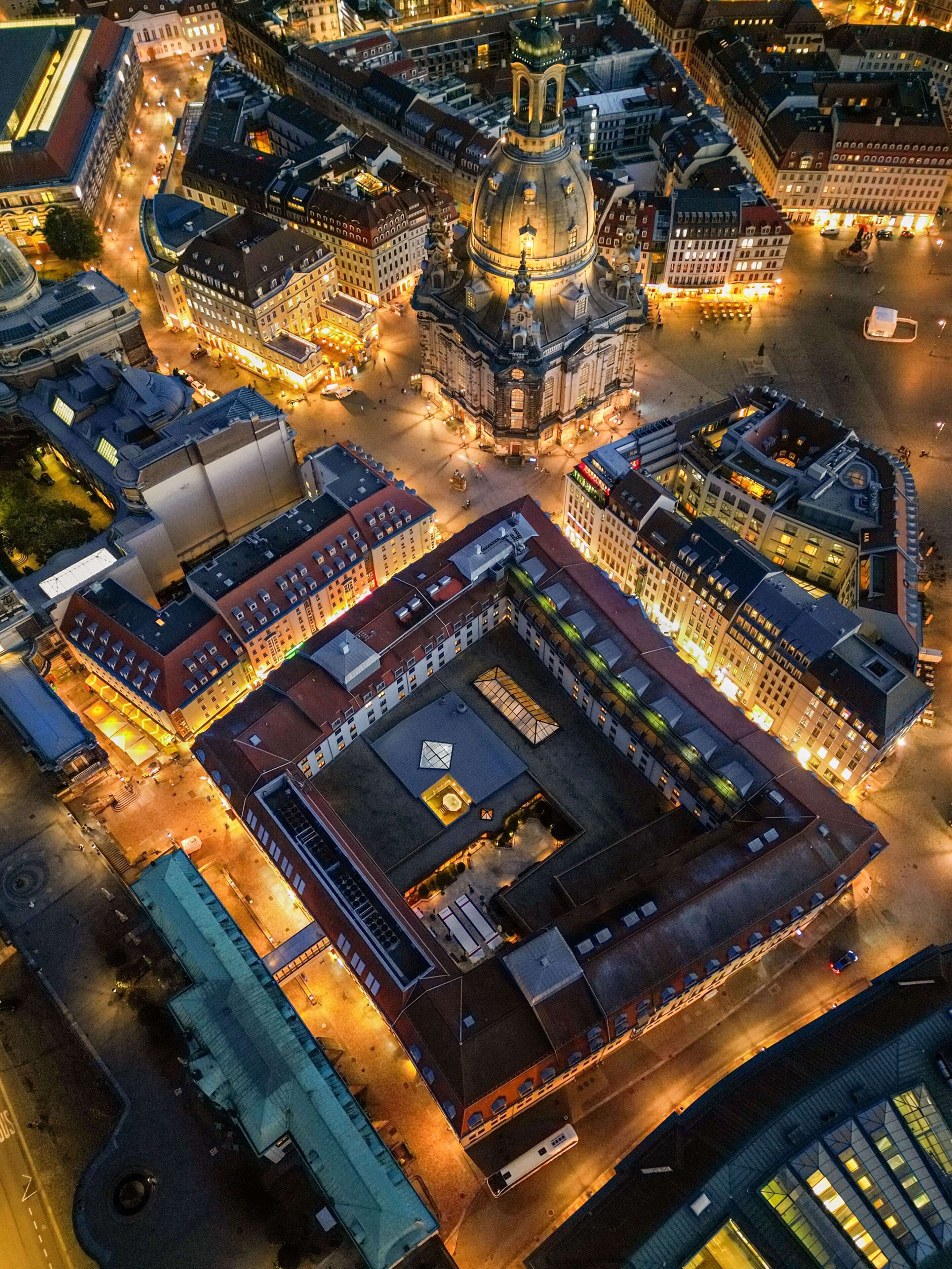An aerial view of a historic city center with a prominent domed building, a large open square, and surrounding modern buildings.