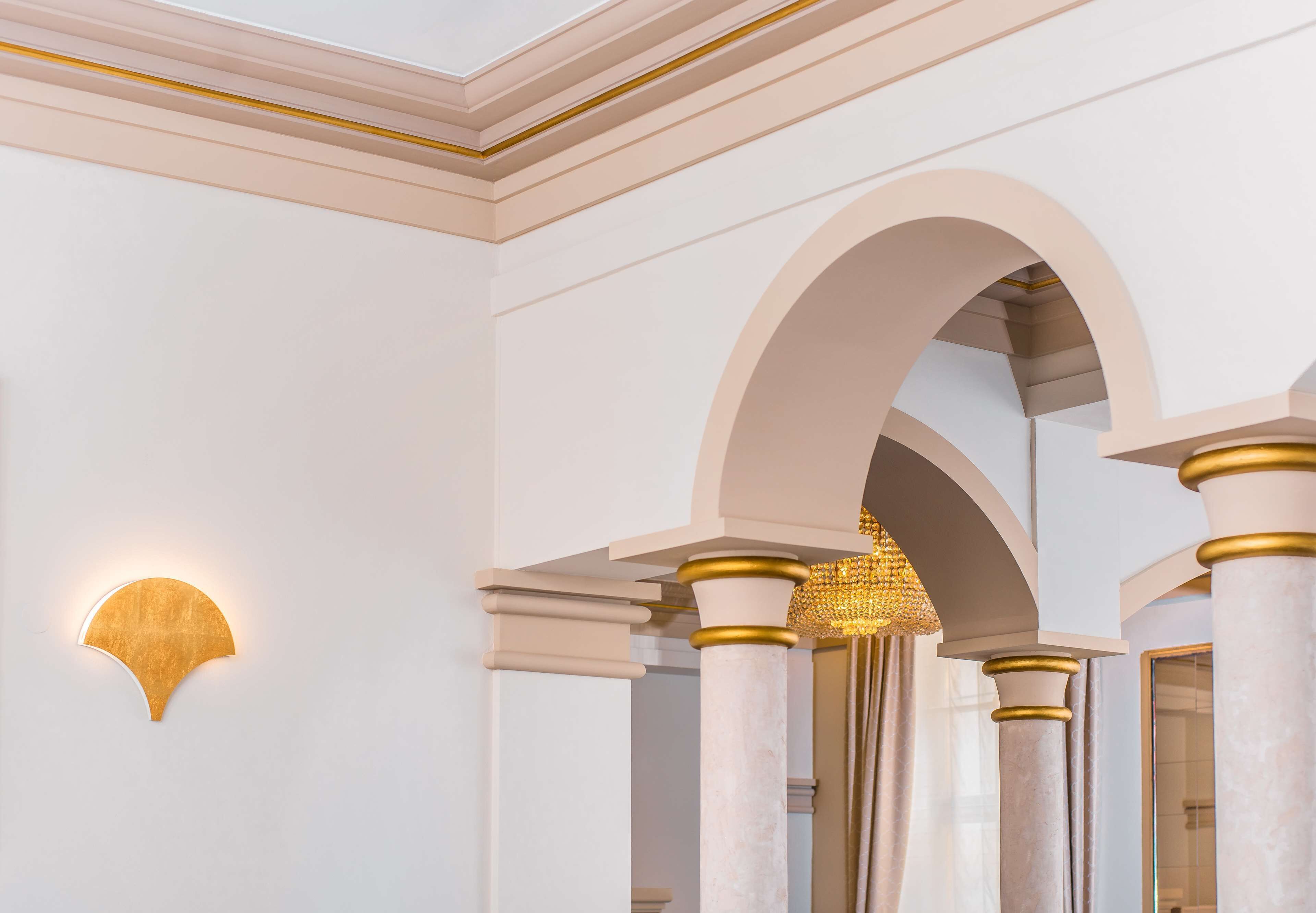 Una habitación con paredes blancas, una lámpara con marco dorado y columnas de mármol.