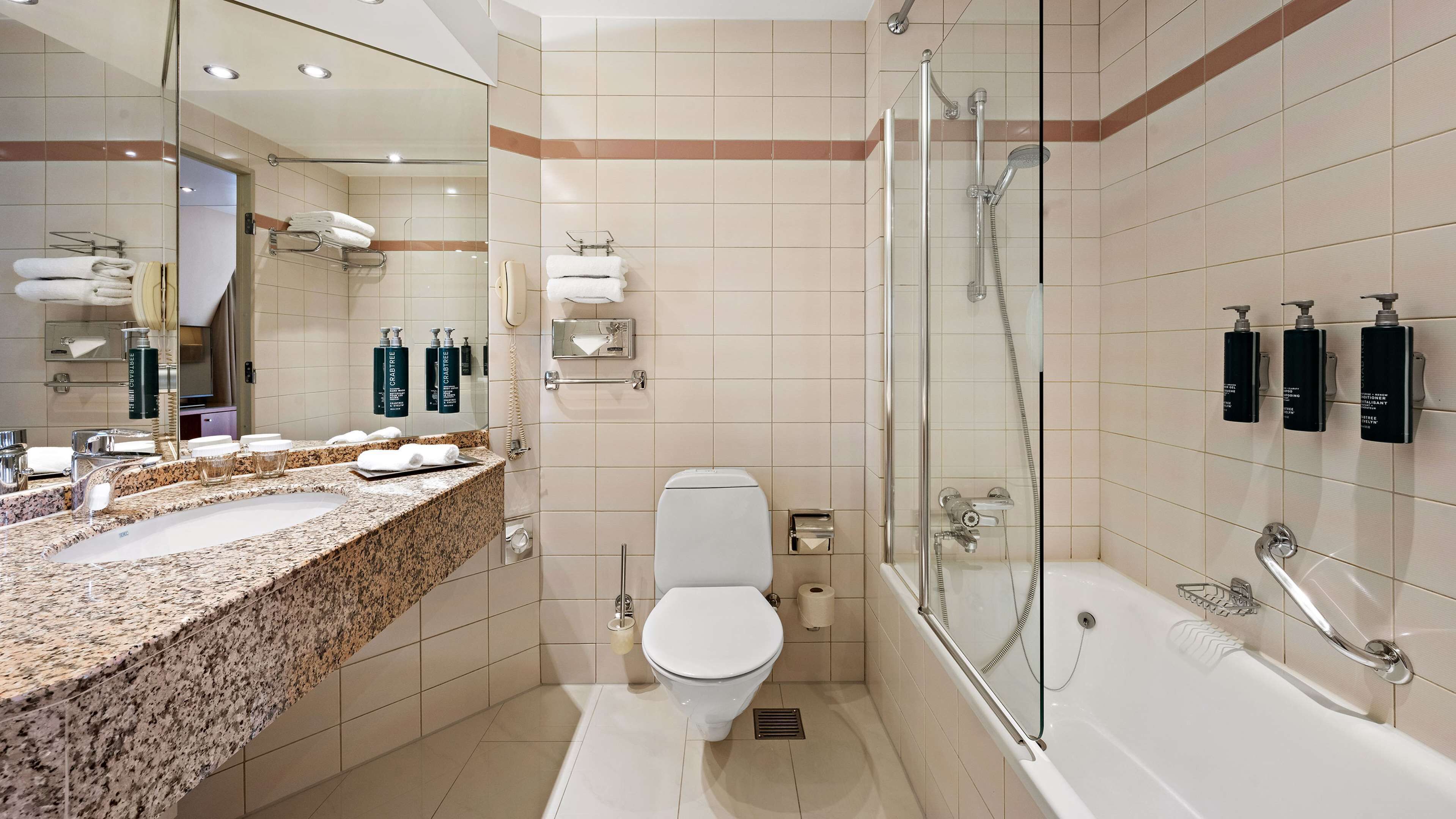 A modern bathroom with a granite countertop, a toilet, a glass-enclosed shower, and a large mirror.